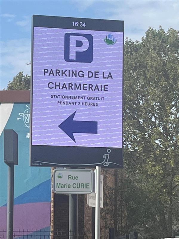 Panneau lumineux violet indiquant « Parking de la Charmeraie — stationnement gratuit pendant 2 heures » avec une flèche vers la gauche.